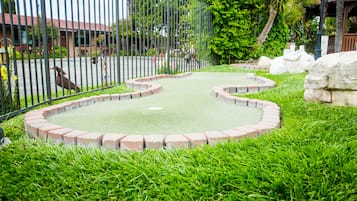 A miniature golf course with a green putting surface, surrounded by a brick border and lush green grass.
