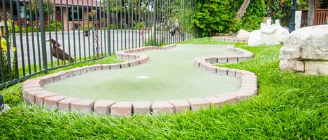 A miniature golf course with a green putting surface, surrounded by a brick border and lush green grass.