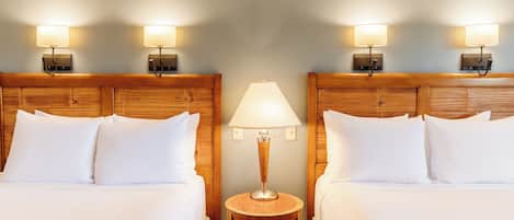 A hotel room with two beds, a round wooden nightstand, and wall-mounted lamps.