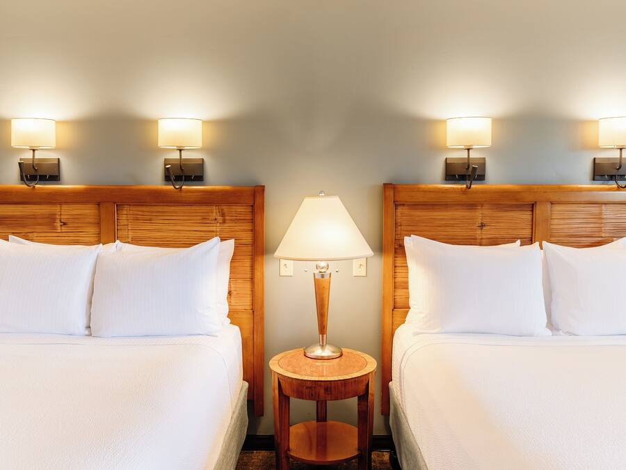 Une chambre d’hôtel avec deux lits, une table de chevet ronde en bois et des lampes fixées au mur.