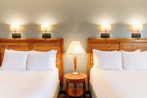 Habitación de hotel con dos camas, una mesita de noche redonda de madera y lámparas fijadas a la pared.