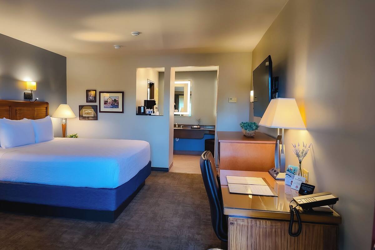 A hotel room with a large bed, bedside lamps, a desk with a telephone, and a mirror.