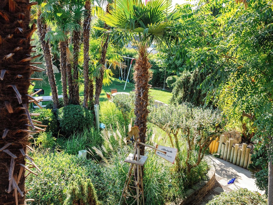 Een weelderige tuin met palmbomen, een bord met daarop Adelaide Motel Inn, en een houten hek.