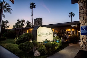 The Adelaide Inn sign with a stone chimney, palm trees, and a clear sky.