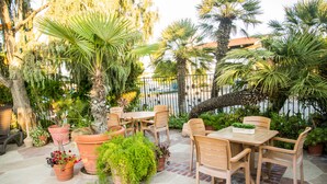 An outdoor patio with a wooden table and chairs, surrounded by potted plants and palm trees. - Adelaide Inn (Paso Robles)
