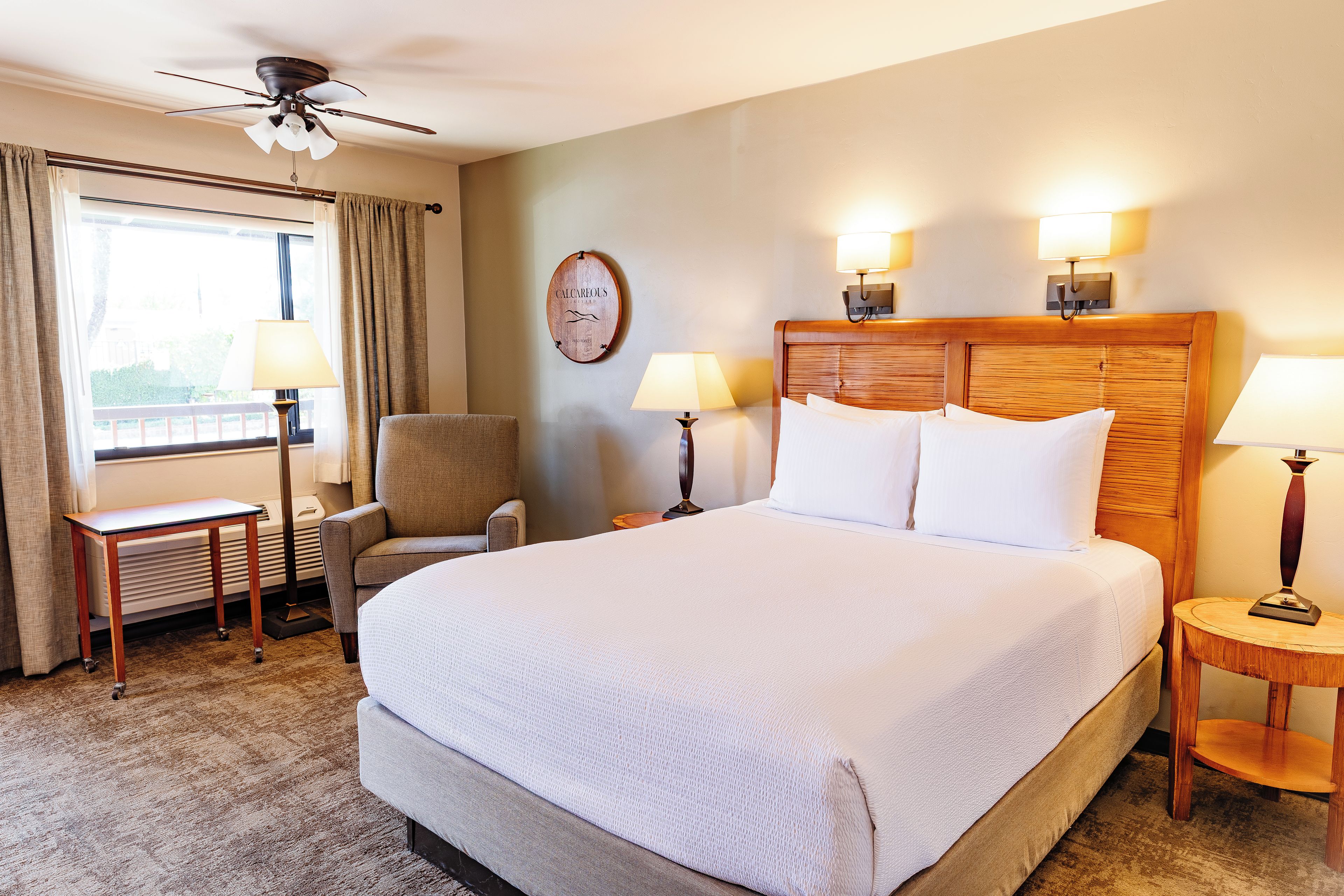 A hotel room with a large bed, a chair, a desk, and a ceiling fan.