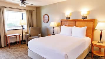 A hotel room with a large bed, a chair, a desk, and a ceiling fan.