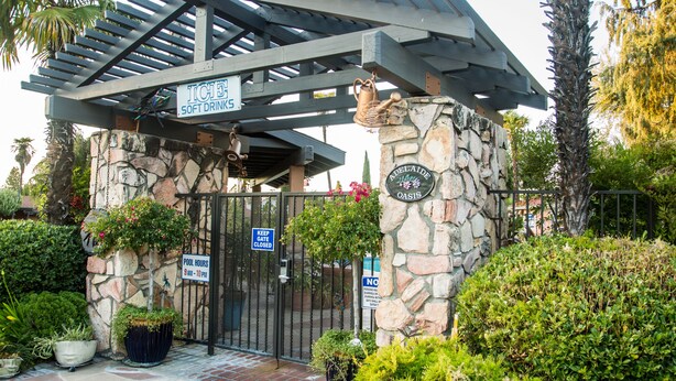 A stone building with a metal gate, a pergola, and signs indicating ice soft drinks and pool hours. - Adelaide Inn (Paso Robles)