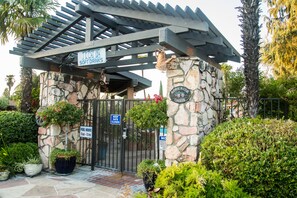 A stone building with a metal gate, a pergola, and signs indicating ice soft drinks and pool hours.