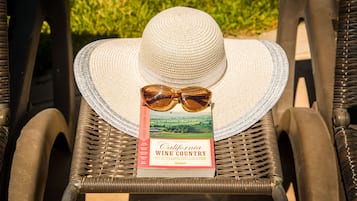 A wicker chair with a straw hat and sunglasses on top, and a book titled "California Wine Country" beside it.