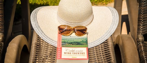 A wicker chair with a straw hat and sunglasses on top, and a book titled "California Wine Country" beside it.