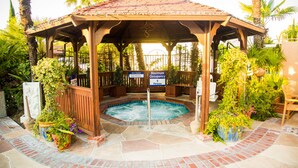 A gazebo with a hot tub, surrounded by potted plants and palm trees. - Adelaide Inn (Paso Robles)