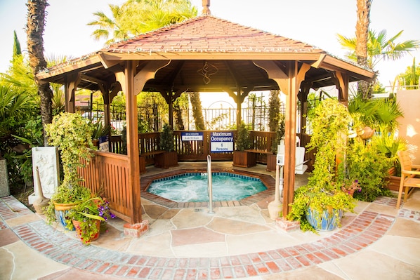 A gazebo with a hot tub, surrounded by potted plants and palm trees.