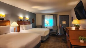 A hotel room with two beds, a desk, a chair, a TV, and a window with curtains. - Adelaide Inn (Paso Robles)