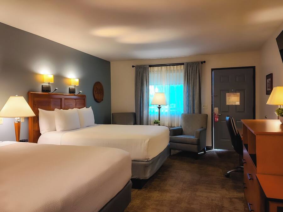 A hotel room with two beds, a desk, a chair, a TV, and a window with curtains.