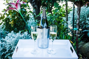 A bottle of champagne in a metallic container with two glasses on a white tray, set against a lush garden backdrop.