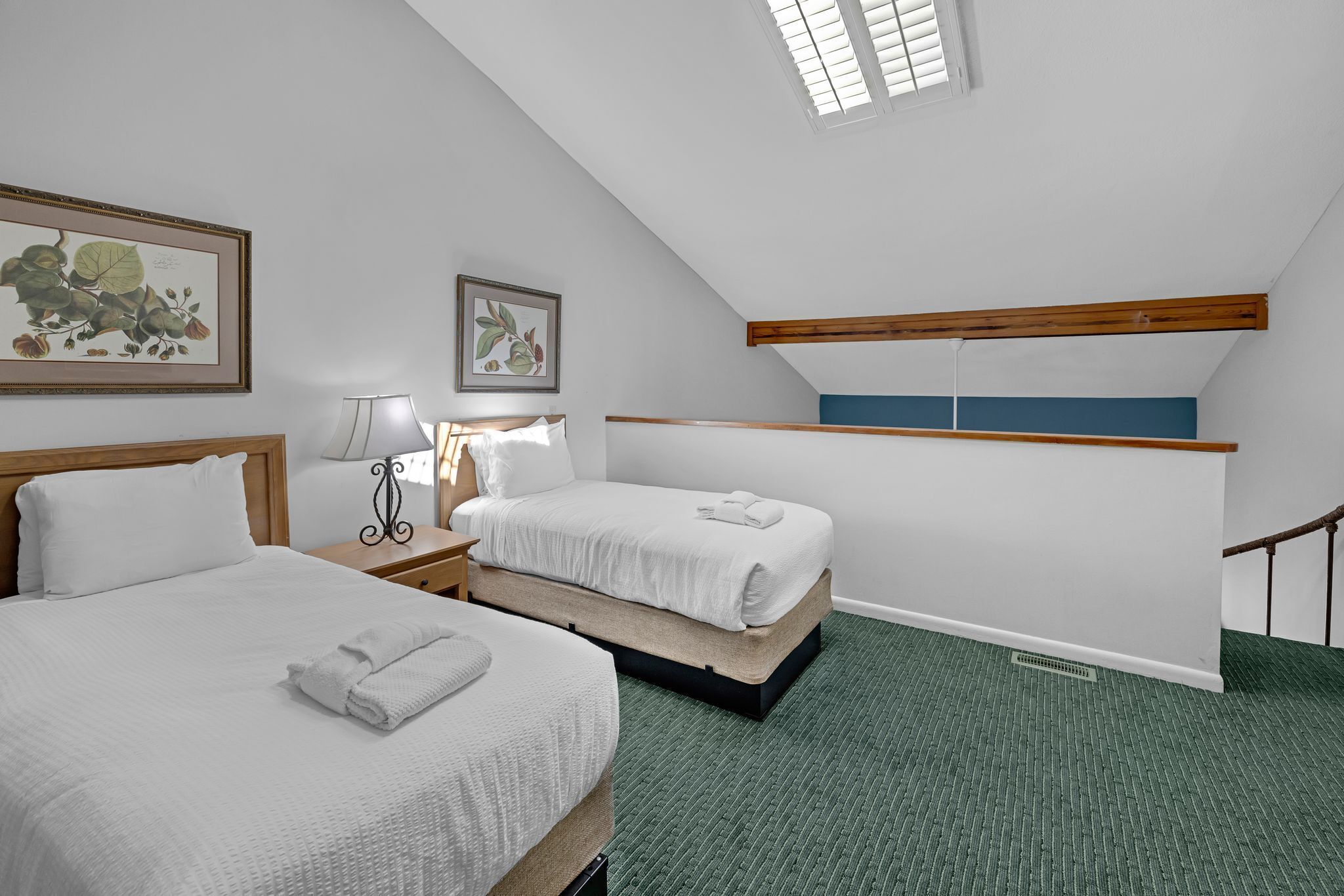 A hotel room with two beds, a desk, a lamp, and a window with blinds.