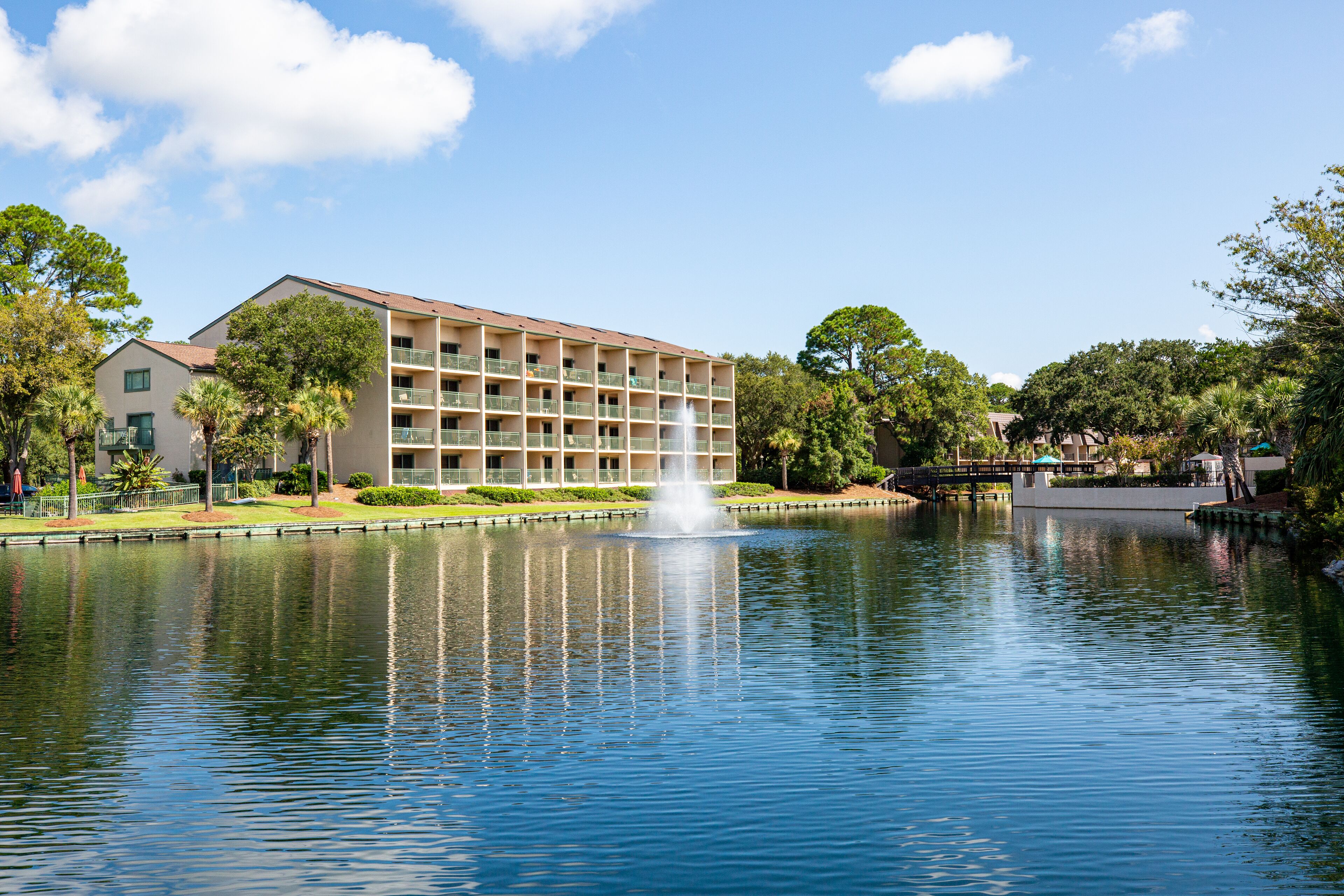 A hotel with a large building, a fountain in the middle of a pond, and surrounding greenery.