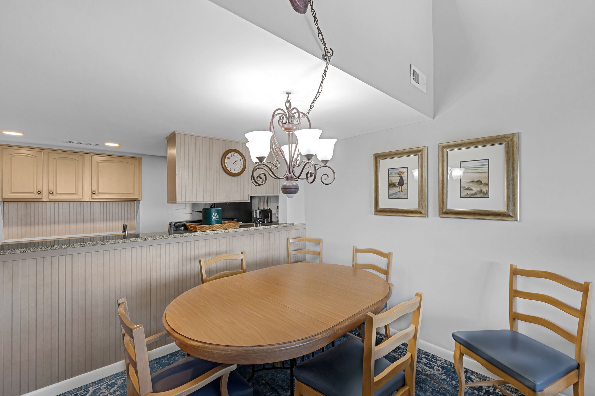 A dining area with a wooden table and chairs, a chandelier, and framed pictures on the wall.