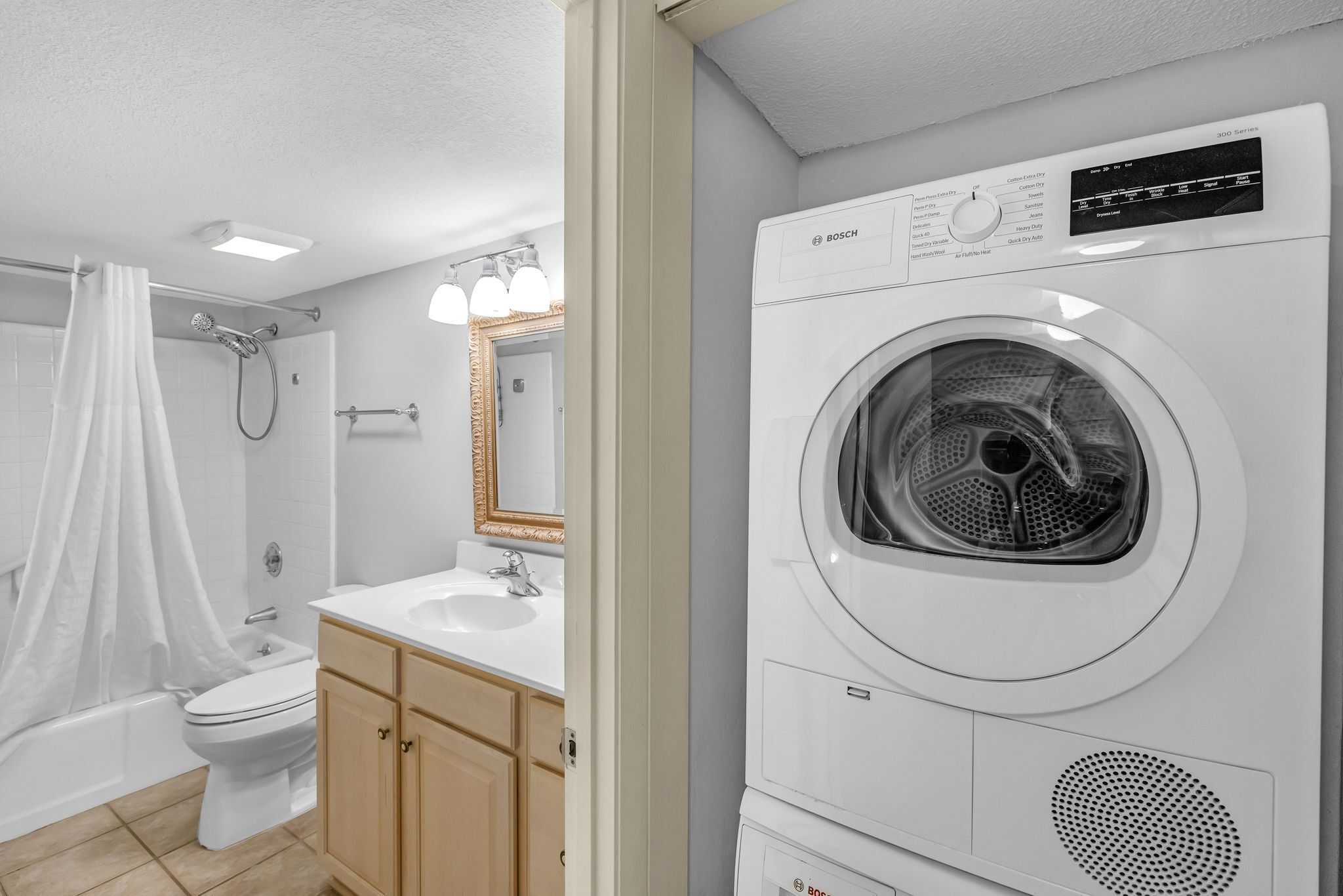 A modern bathroom with a Bosch washing machine, a toilet, a sink, and a shower with a curtain.