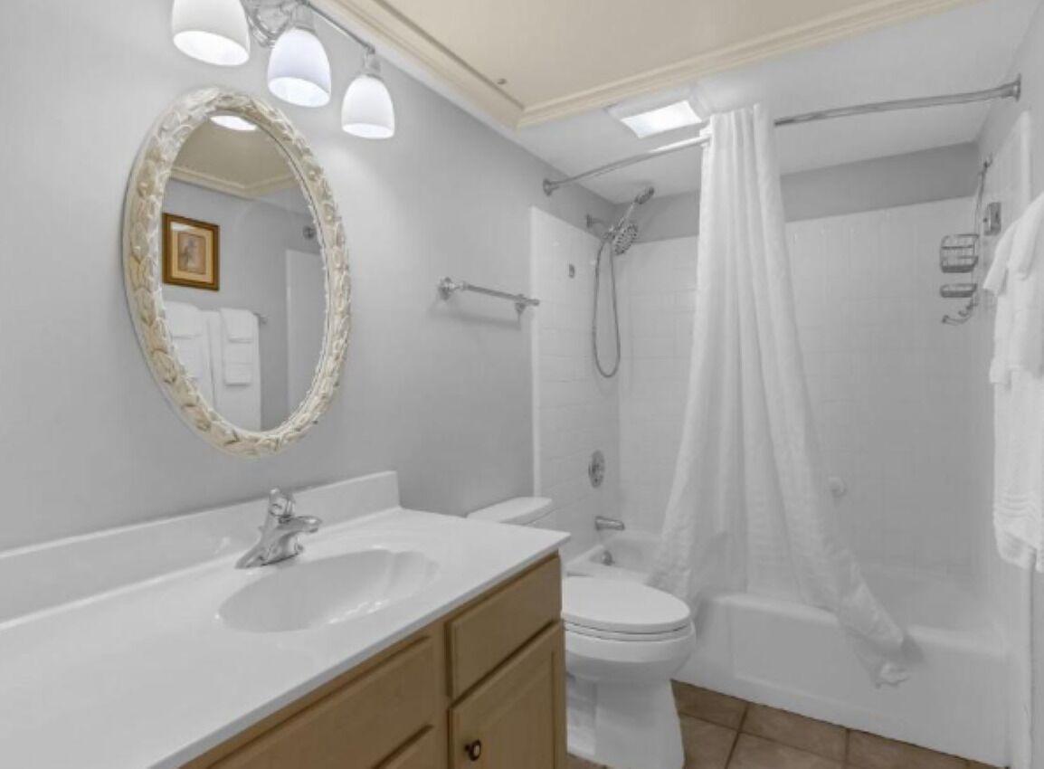 Un baño con lavamanos, inodoro, ducha y un espejo con marco decorativo.