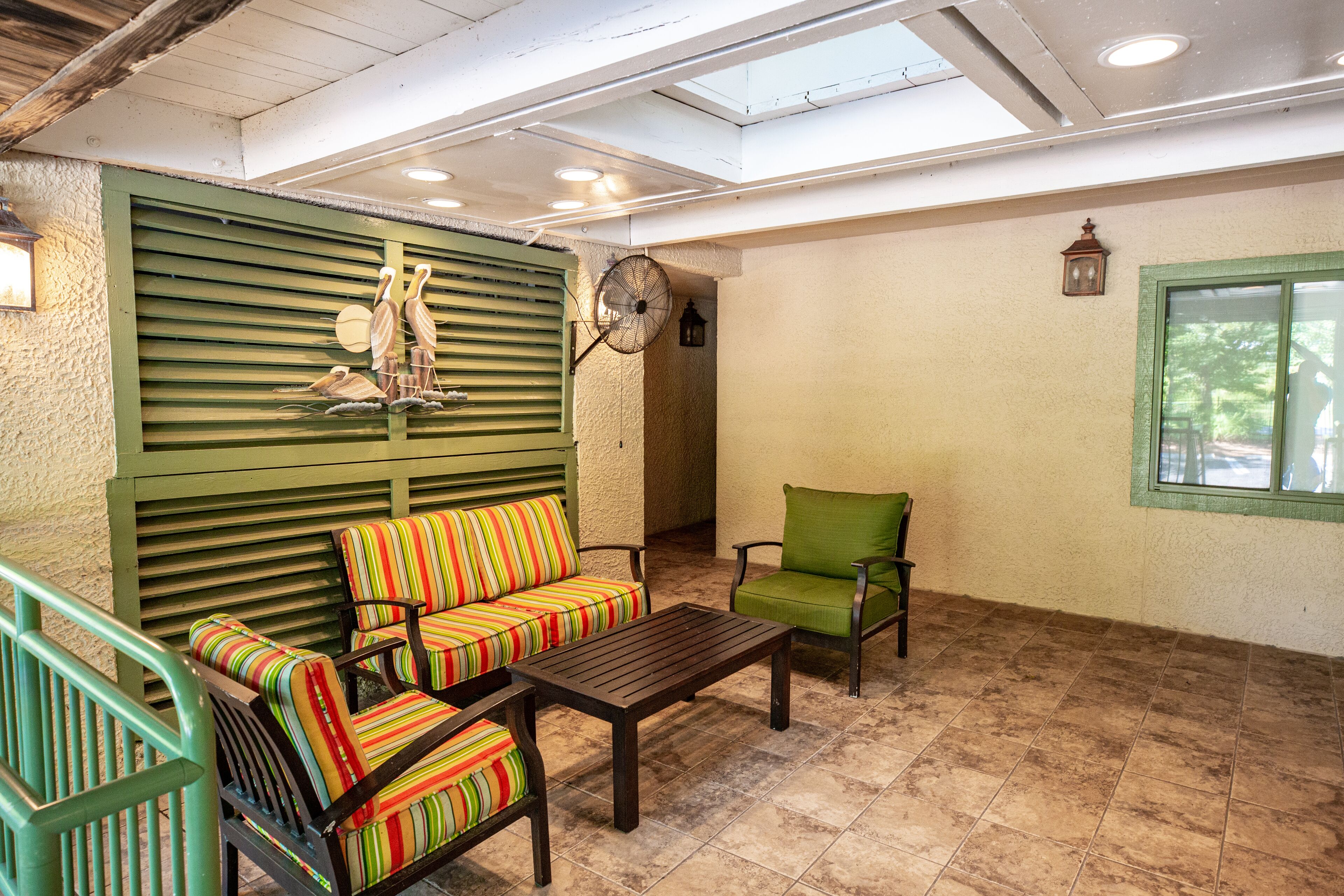 A covered patio area with a wooden table, striped chairs, and a green cushioned bench.