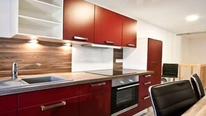 Una cocina moderna con gabinetes rojos, un lavamanos de acero inoxidable y un horno empotrado.