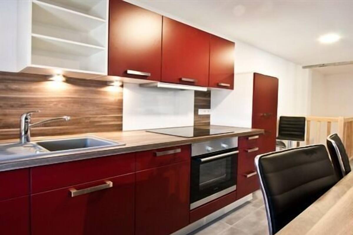 A modern kitchen with red cabinets, a stainless steel sink, and a built-in oven.
