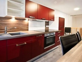Una cocina moderna con gabinetes rojos, un lavamanos de acero inoxidable y un horno empotrado.