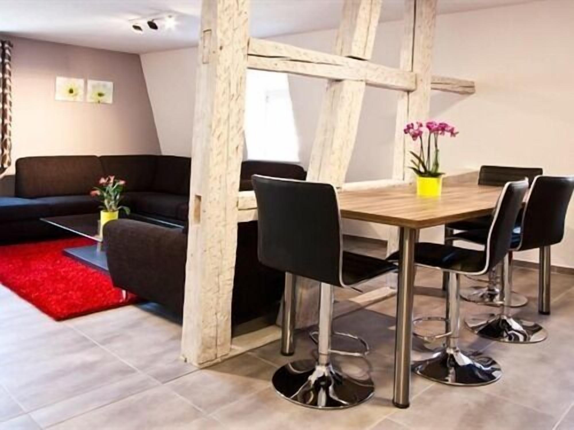 Een moderne woonkamer met een houten eettafel, zwarte stoelen, een rode vloerkleed en een zwarte bank.