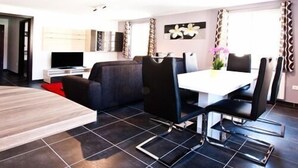Una sala de estar moderna con comedor, que incluye un sofá, un televisor y una mesa de comedor con sillas.