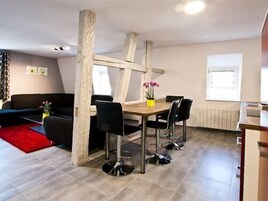 Una sala de estar moderna con comedor, que presenta una mesa de madera, sillas negras y un tapete rojo.