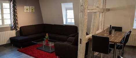 A modern living room with a sectional sofa, a dining table with chairs, a red rug, and a wooden partition.