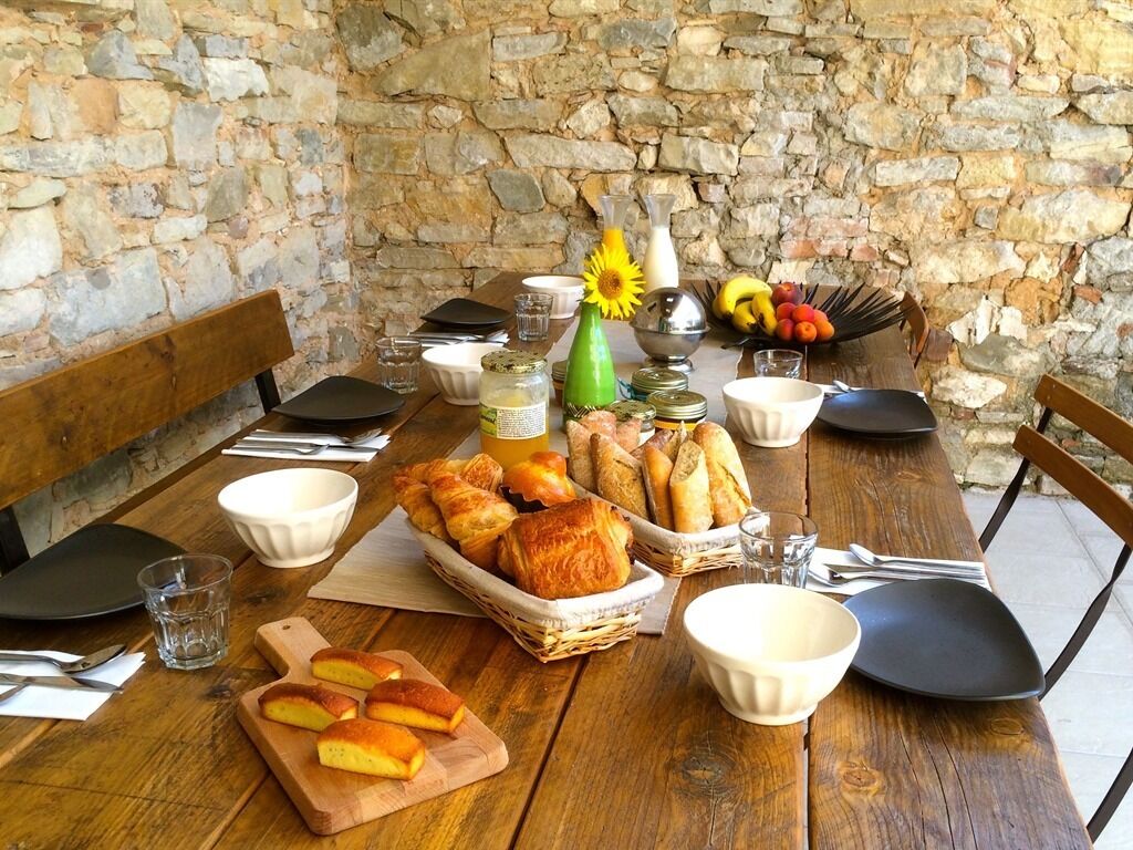 Una mesa rústica dispuesta con pan, frutas y aderezos, rodeada de paredes de piedra.