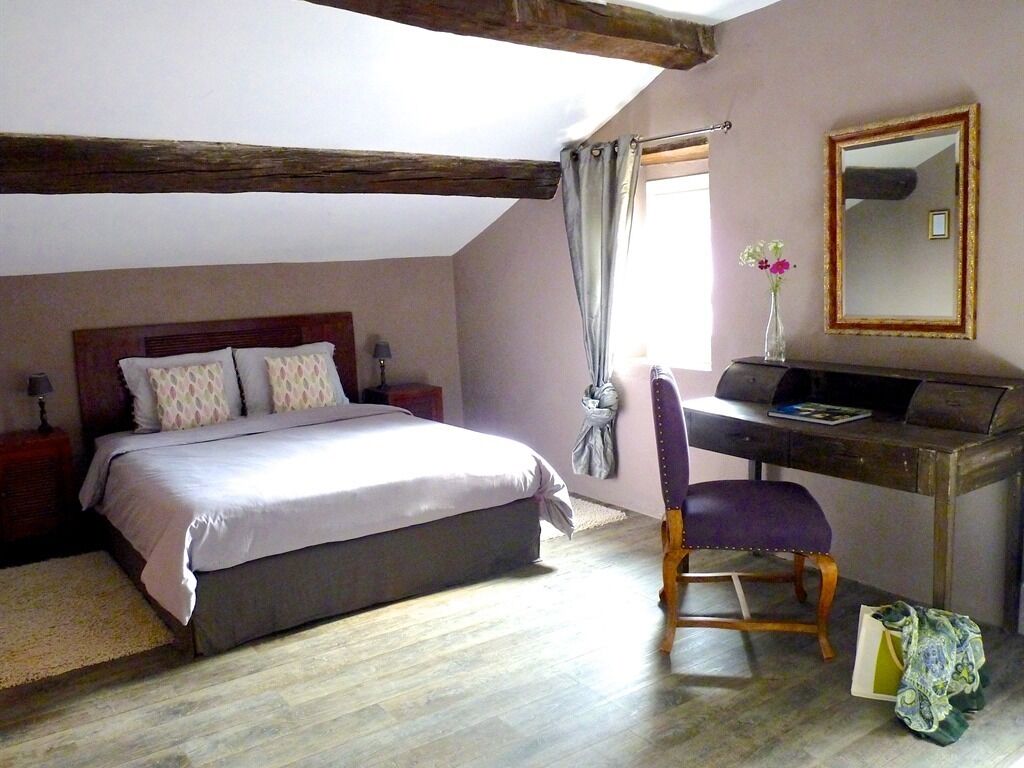 Une chambre à coucher avec un lit, un bureau, une chaise, un miroir et une fenêtre avec des rideaux.