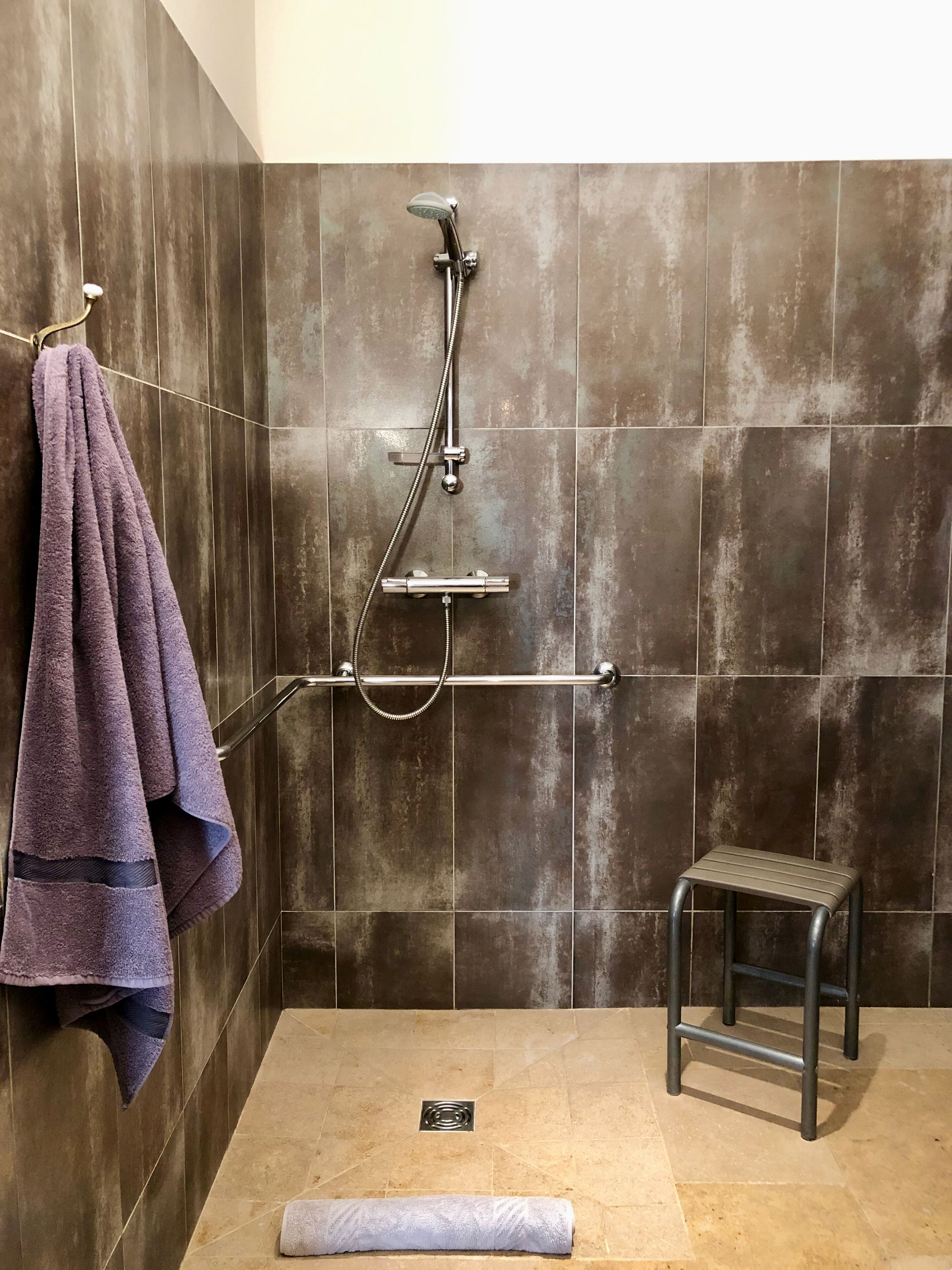 A shower area with a handheld showerhead, a towel rack with a purple towel, and a small stool.