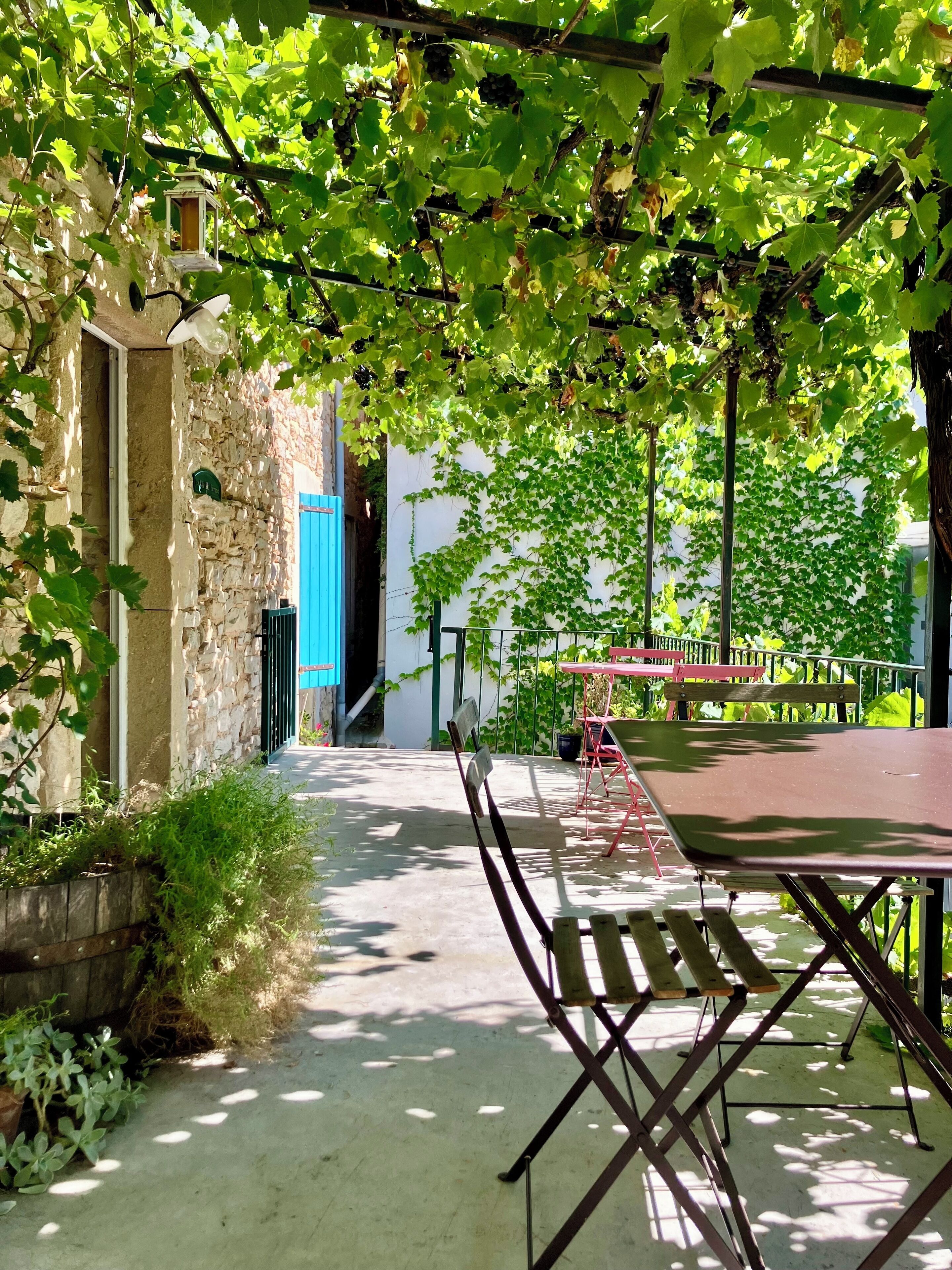 A covered outdoor area with a table and chairs, stone walls, and greenery.