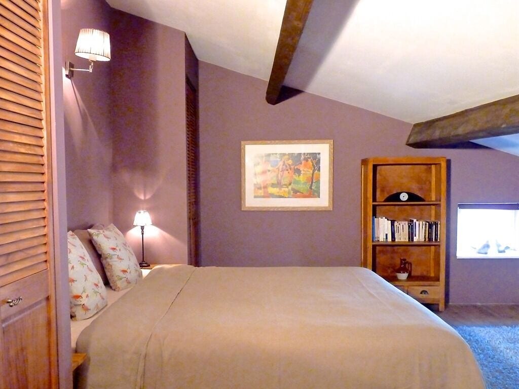 Une chambre à coucher avec un lit, une table de chevet, une lampe, une bibliothèque et une fenêtre.