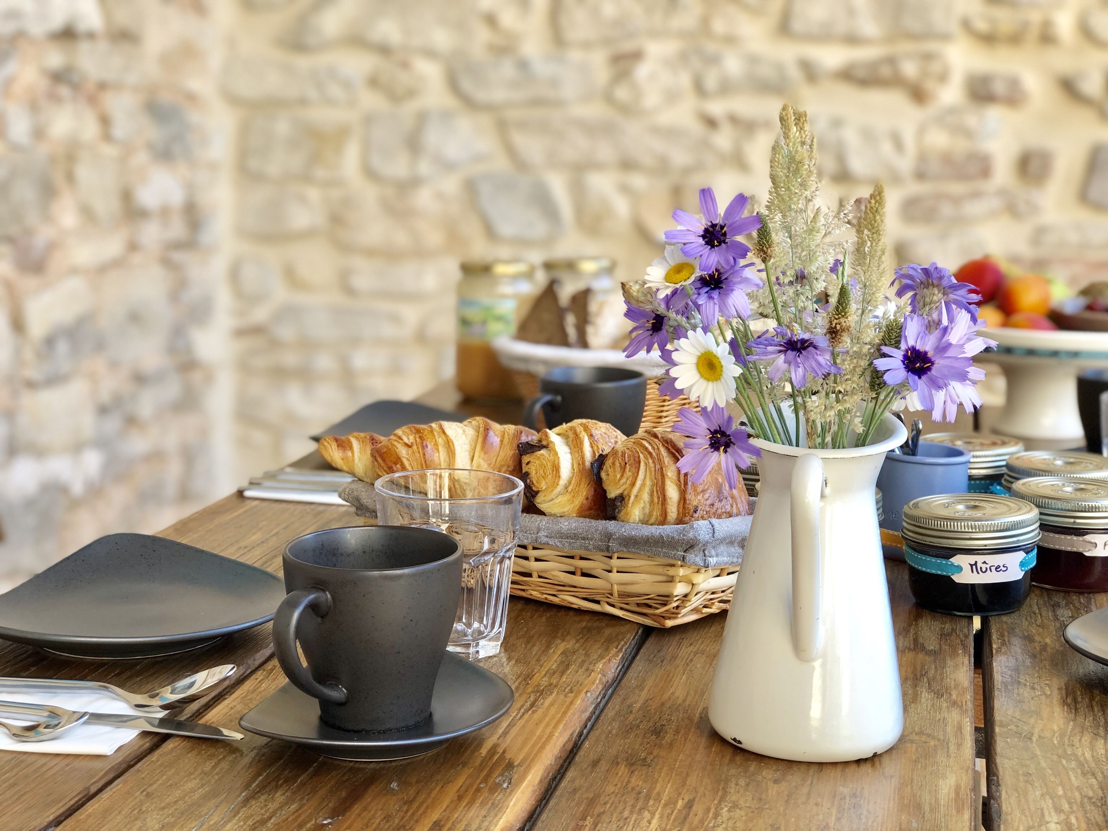 A breakfast table with croissants, a vase of flowers, a cup, and a basket.