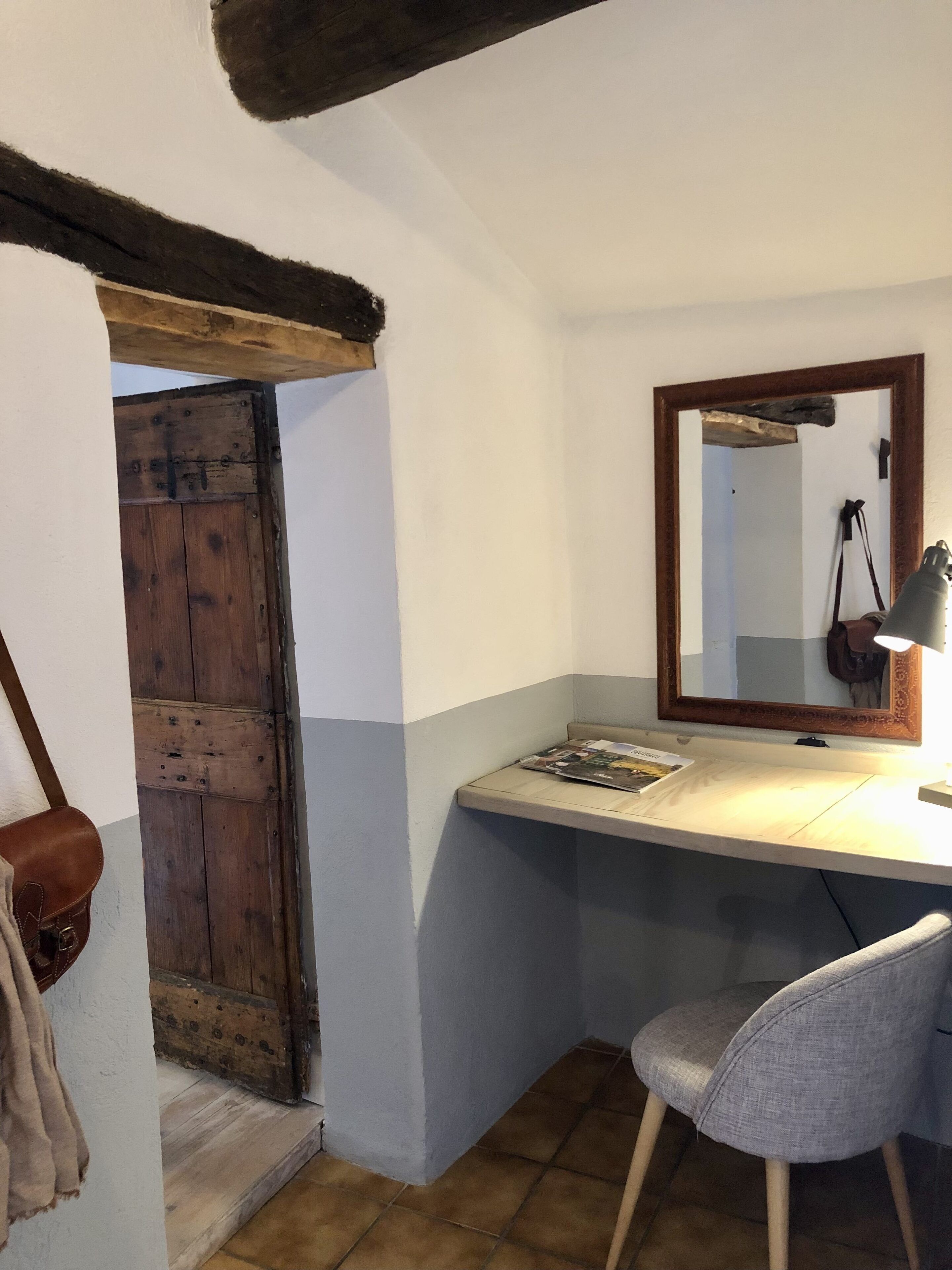 Een kleine, knusse kamer met een houten deur, een bureau met een lamp en een stoel.