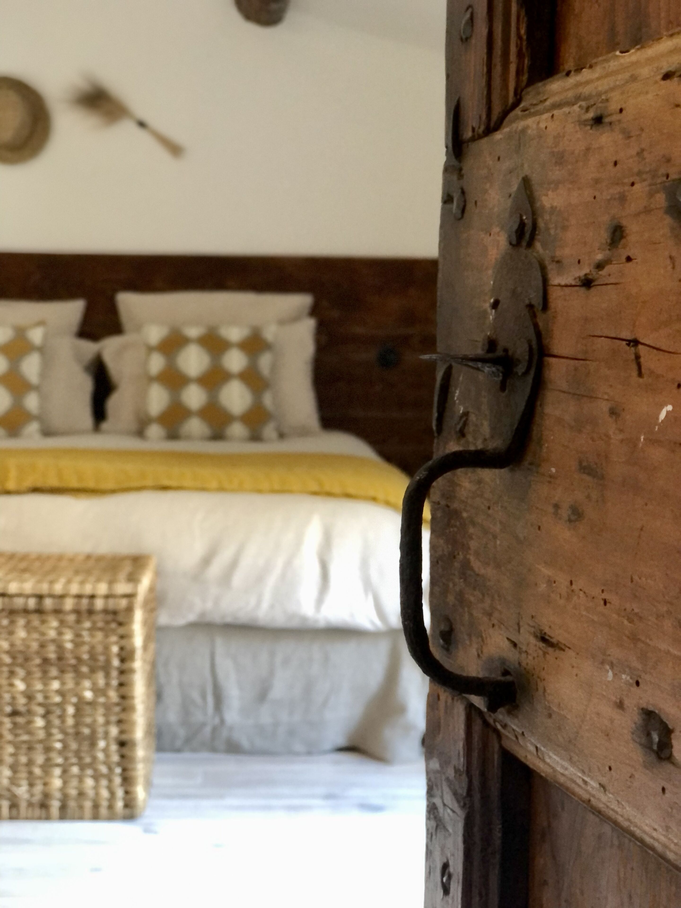 A rustic wooden door with a metal latch, a bed with white bedding and patterned pillows, and a woven basket on the floor.