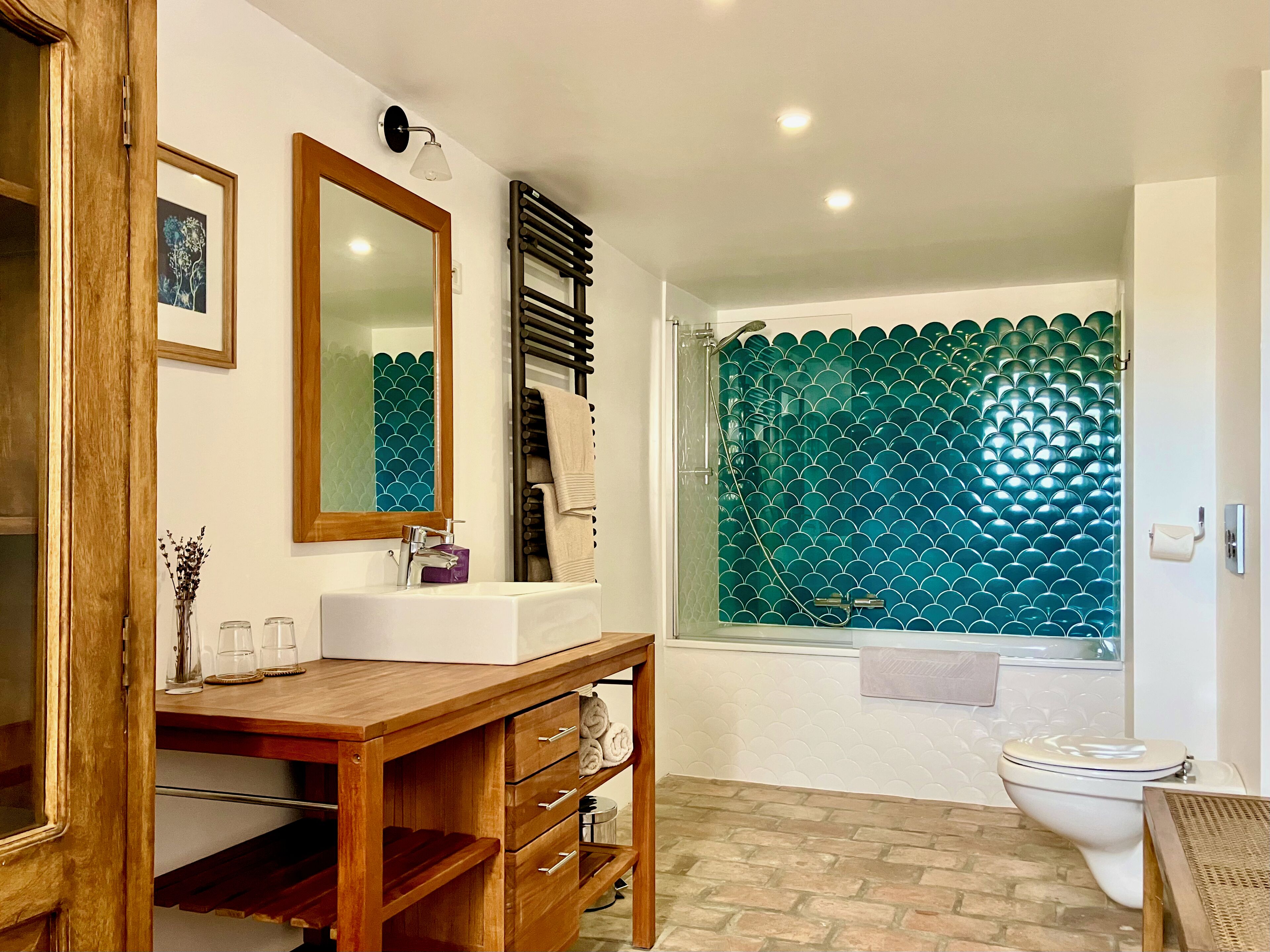 A bathroom with a wooden vanity, a white sink, a mirror, a towel rack, and a shower with a green tiled wall.
