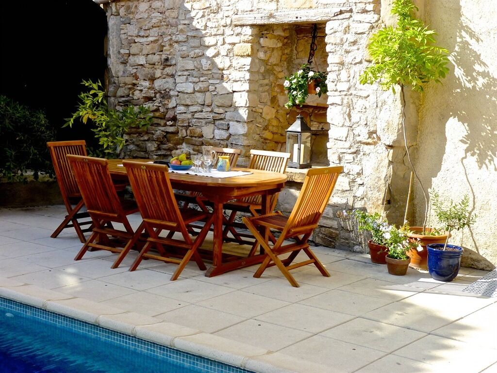 An outdoor dining area with a stone wall, wooden table, and chairs.