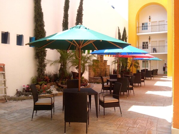 An outdoor patio area with multiple tables and chairs, some shaded by umbrellas. - Happy Express Hotel (Oaxaca)