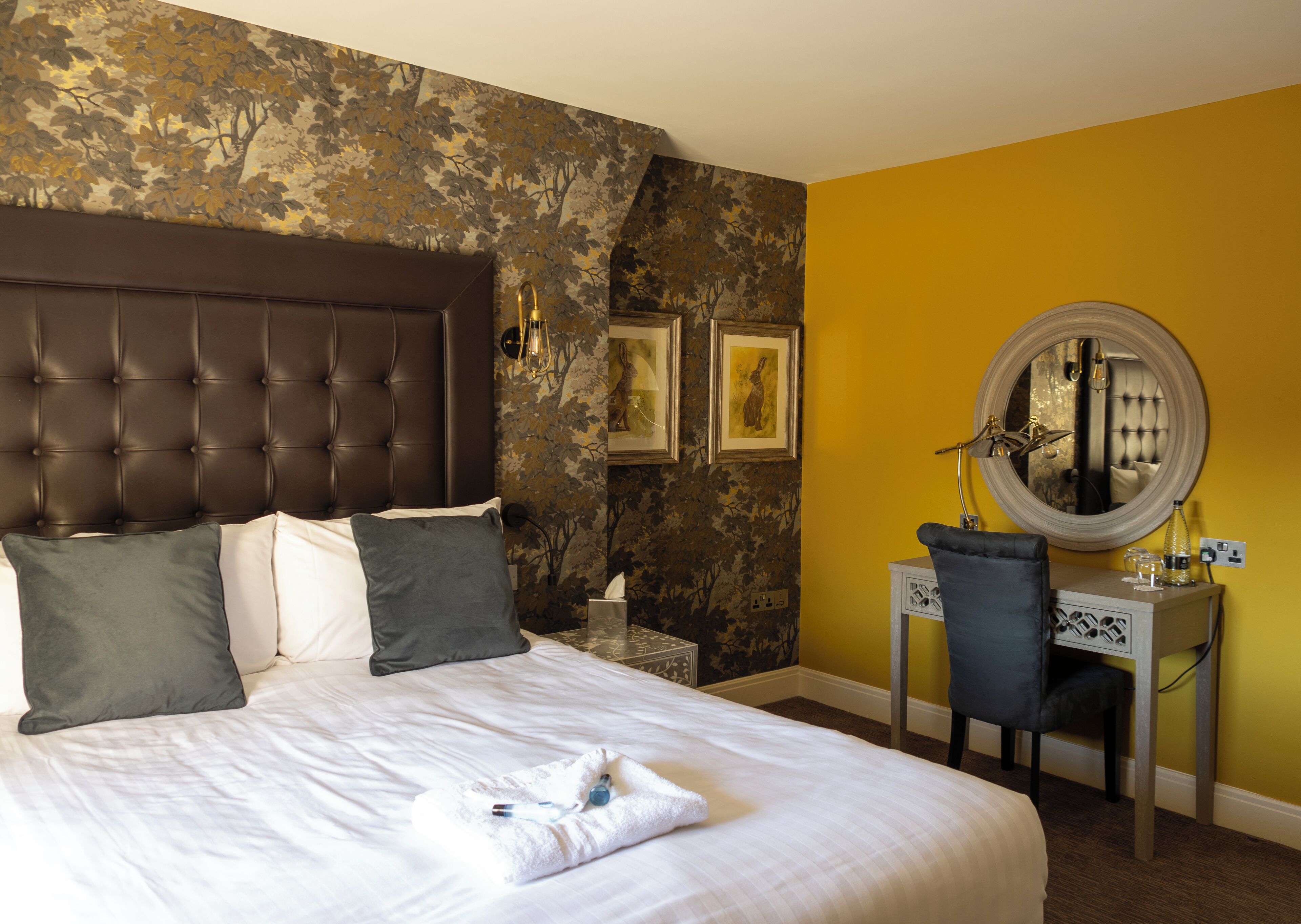 A hotel room with a large bed, a desk, a chair, and a mirror.