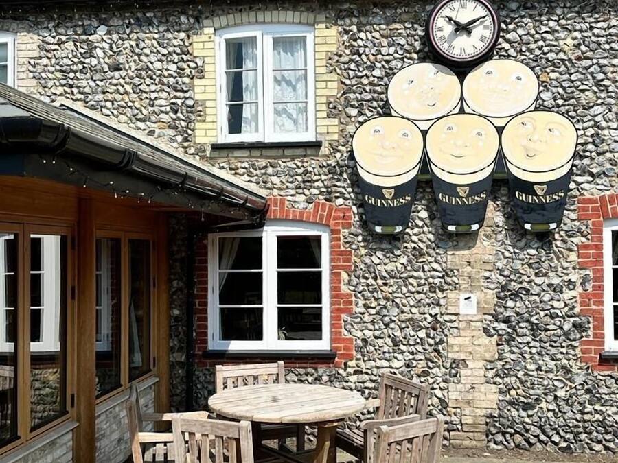 Un edificio de piedra con un reloj, barriles de cerveza Guinness y una mesa de madera con sillas.