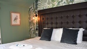 Ein ordentlich bezogenes Bett mit Kissen, ein gerahmtes Vogelbild an der Wand und eine Wand mit einem Blattmuster.