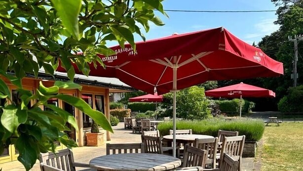 Eine Terrasse im Freien mit Holztischen und -stühlen, roten Sonnenschirmen und einem Fliesenboden aus Stein.