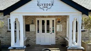 Der Eingang des Elveden Inn mit einer Steinfassade, weißem Zierwerk und einem Schild über der Tür.