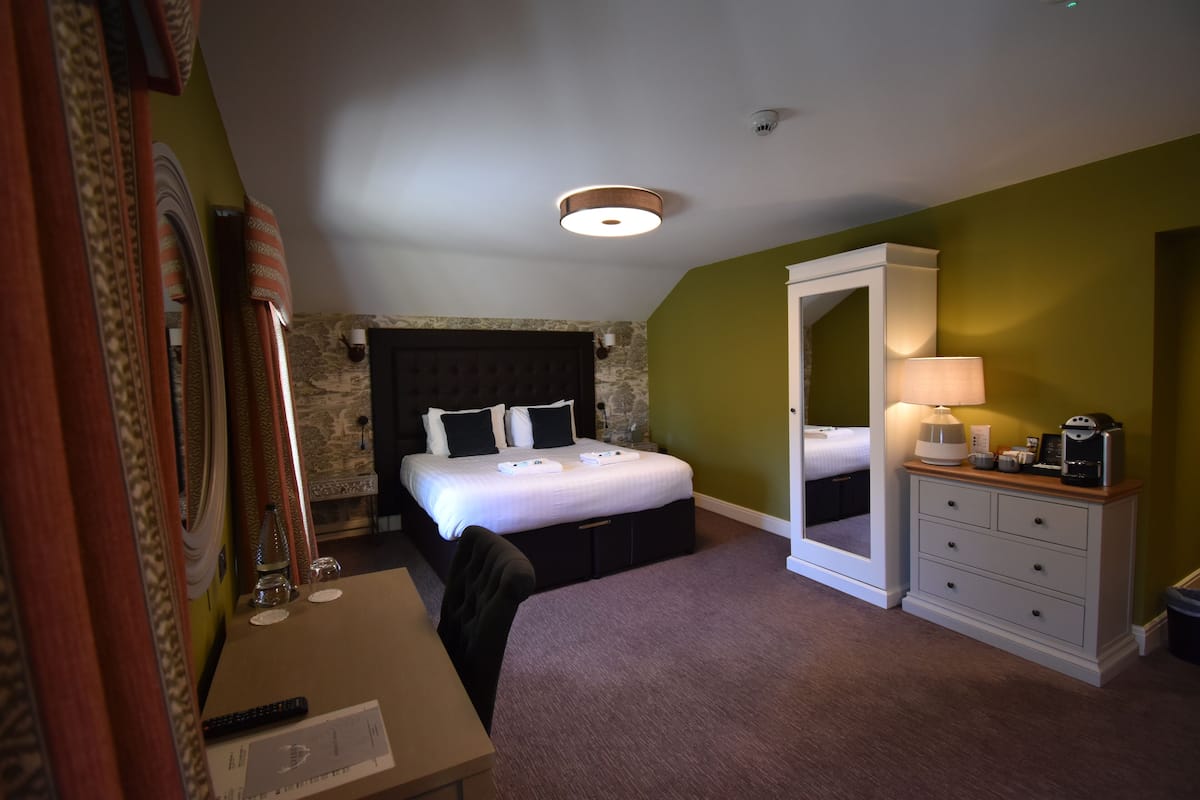 A hotel room with a bed, a desk, a dresser, a mirror, and a lamp.